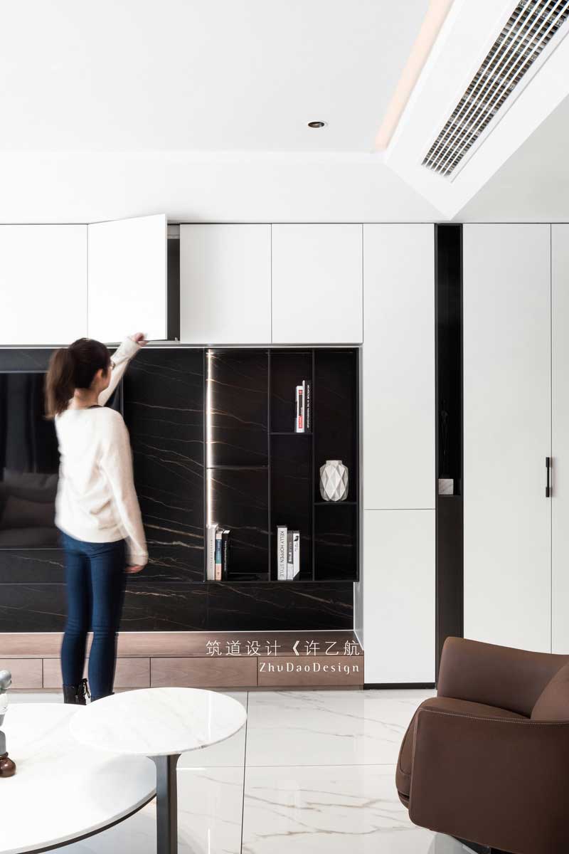  設(shè)計師拋棄傳統(tǒng)客廳的固有印象，將儲物柜與電視背景墻相結(jié)合，不僅增加了空間的儲物空間，在自然柔和的燈帶的襯托下，深灰色的啞光金屬條與深色大理石背景更有層次感，也成為了公共空間的一亮點(diǎn)所在。