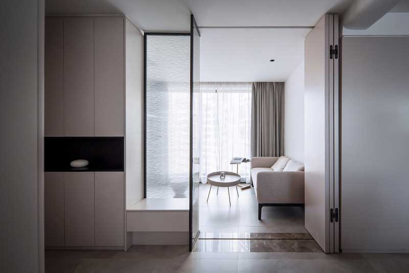 打破原有入戶花園格局限制 重新拆解再利用 利用頂天立地的鞋柜與折疊門結合，磨砂玻璃隔斷下的小臺子兼任換鞋凳的功能，光從磨砂玻璃隔斷透出來，即滿足儲物需求，又為女業主從事地產行業需要在家辦公筑建一個多功能的空間，營造一個開闊又多變的開敞交互的家。